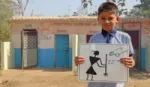 A schoolboy stands in front of a block of toilets holding a hand-drawn poster