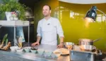 Michelin-starred chef Gregory Marchand stands behind a kitchen worktop bowls of a variety of ingredients