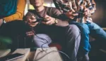 Photo focused in on the hands of three people sitting on a sofa using games consoles to play an online game